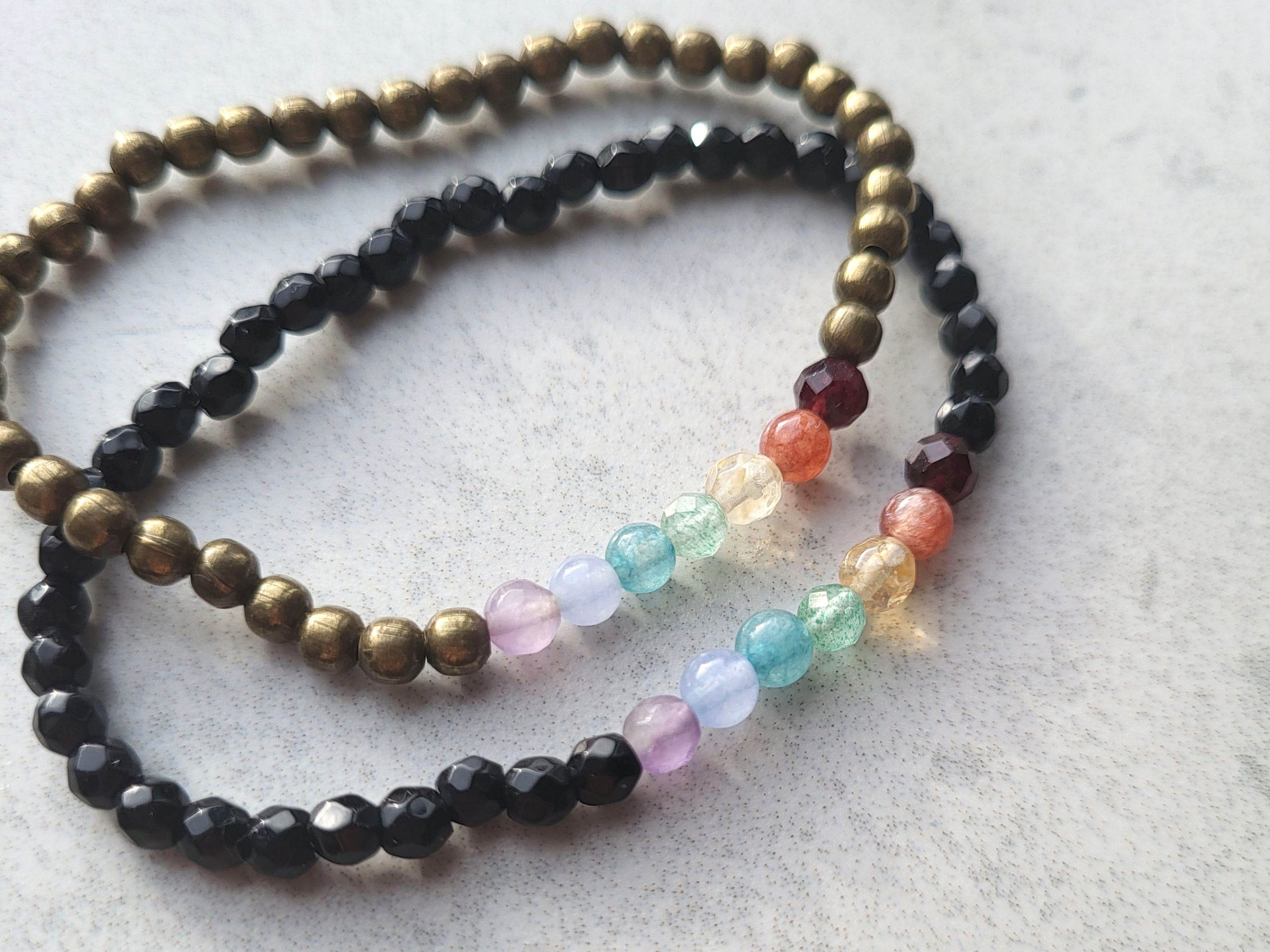 Chakra bracelets in an up close picture to show rainbow colours and details of beads. Two different styles in antique bronze and facet black beads. Sold at earthandharmony.ca