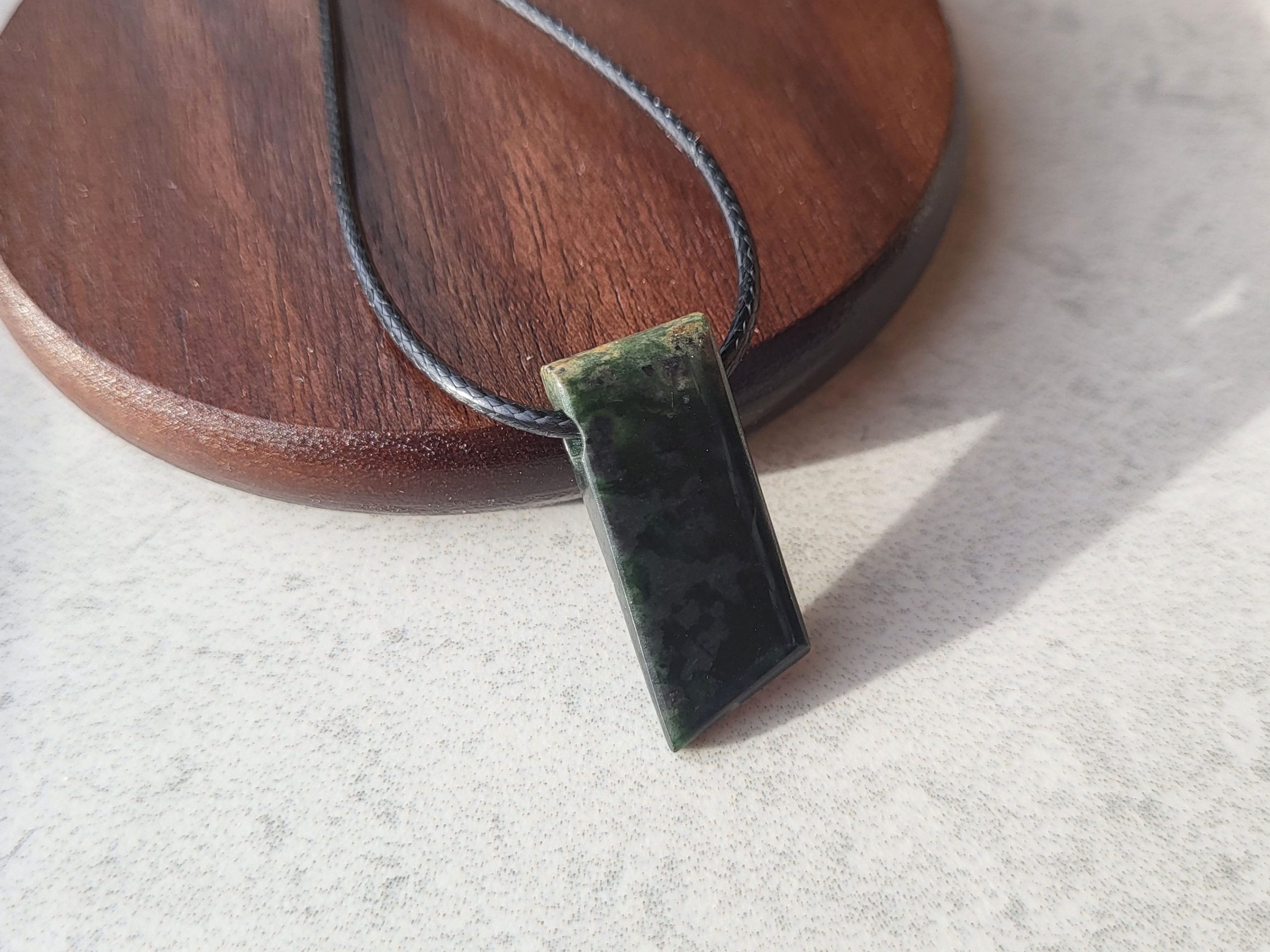 Up close image of Nephrite Jade pendant with black, wax-braided leather cord at front view.