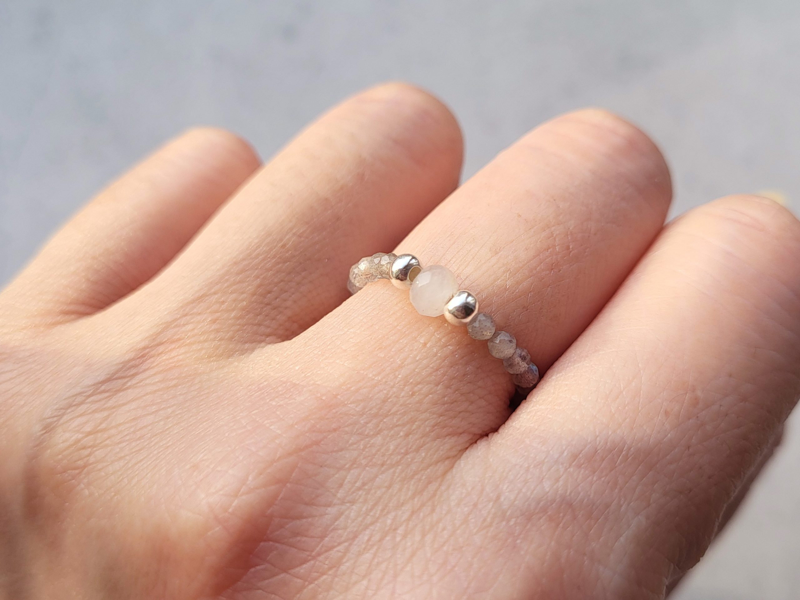 Up close image of a stretch ring made with a single facet white jade bead, two 925 sterling silver beads, and labradorite beads. It is worn on a model's hand to show how it will look when put on. Sold at earthandharmony.ca