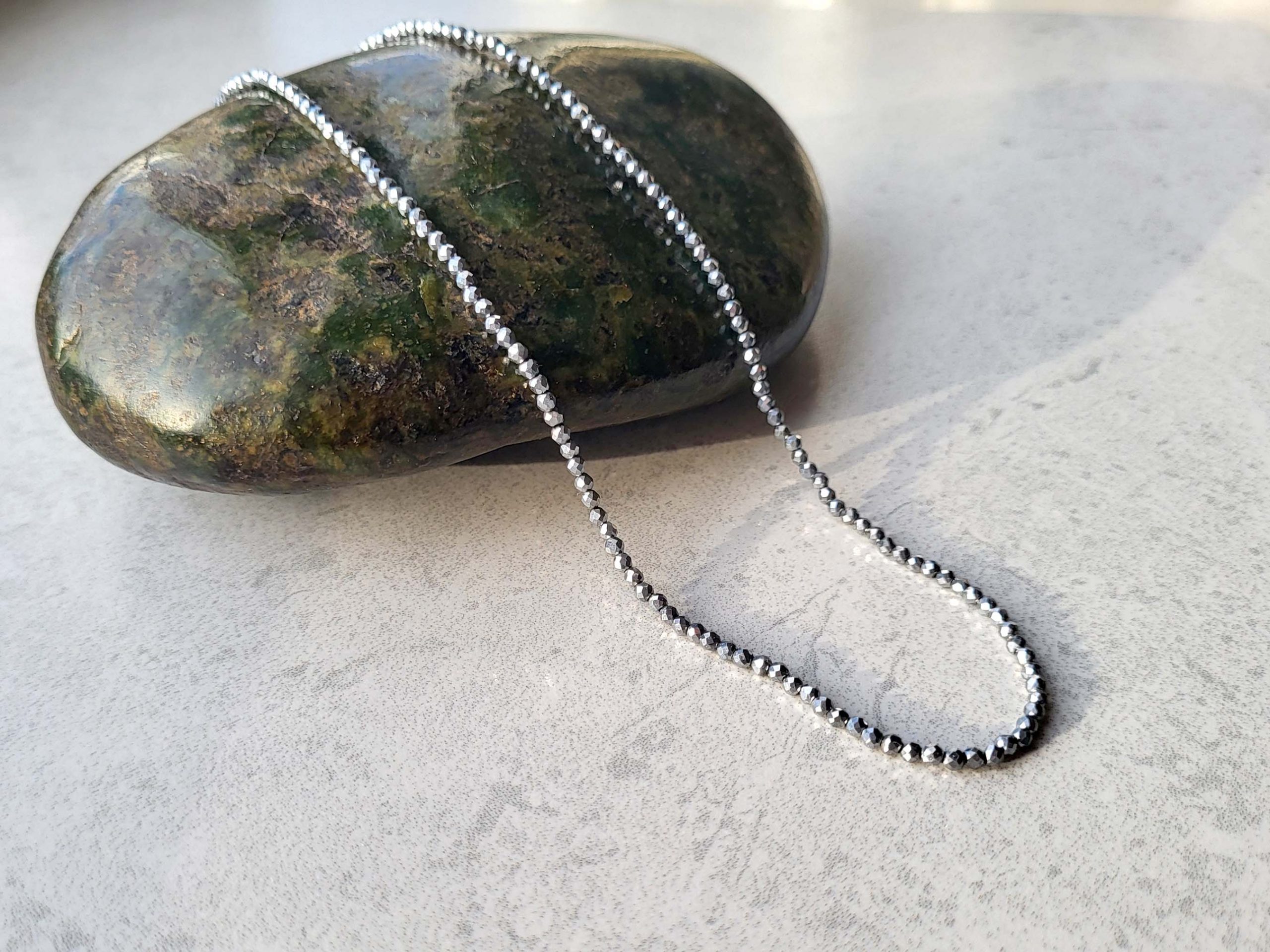 Silver metallic spinel necklace draped over a Serpentine stone.